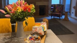 A cozy room with a fireplace, a wooden table with snacks, and a vase of flowers. - Urban Lofts, Melksham - Butler (Melksham)