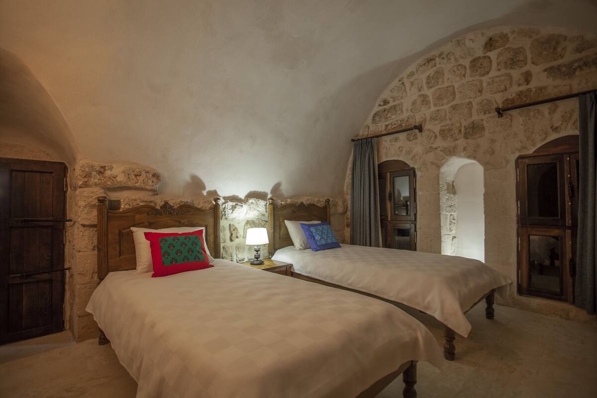 Una habitación con dos camas, paredes de piedra, muebles de madera y un arco de piedra.