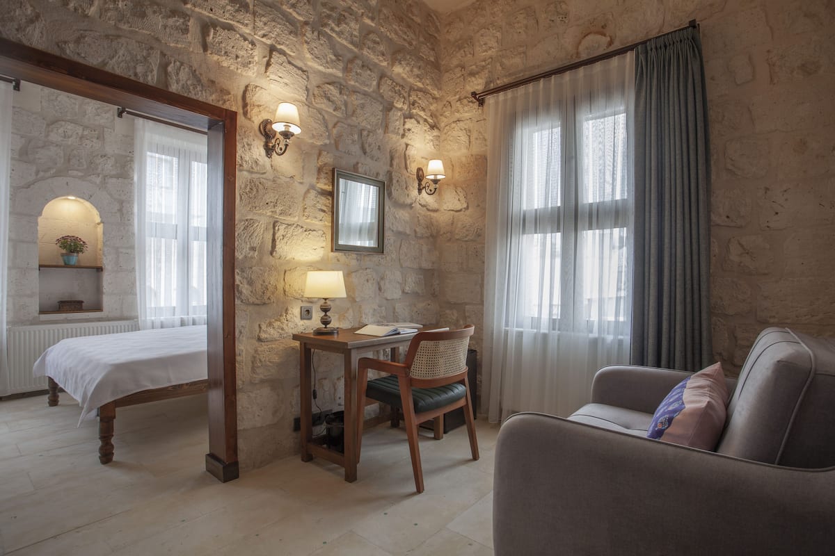 Una habitación con pared de piedra, una cama, un escritorio con silla, un sofá y una ventana con cortinas.