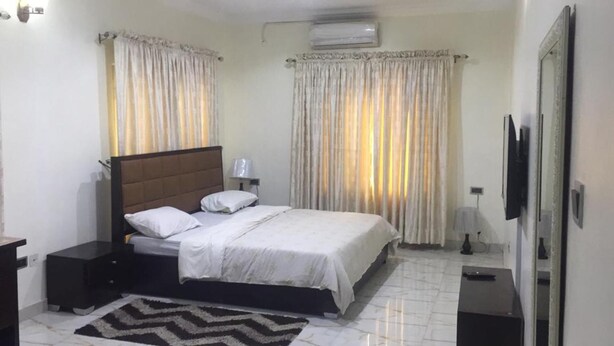A neatly arranged bedroom with a bed, bedside tables, a TV, and curtains. - Stunning 2-bed Apartment in Lagos (Lagos)