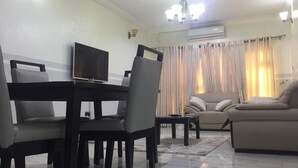 A living room with a dining area, a sofa, a TV, and curtains. - Stunning 2-bed Apartment in Lagos (Lagos)