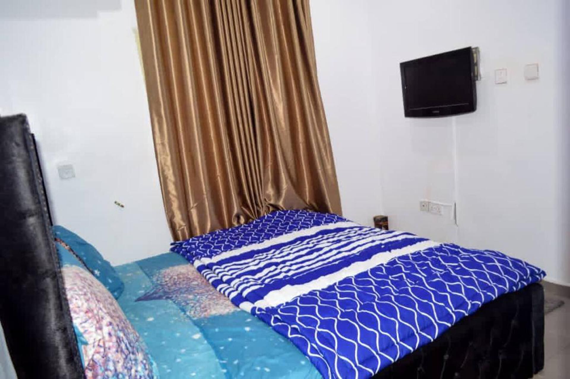 Un dormitorio con cama, televisión montada en la pared y una cortina.