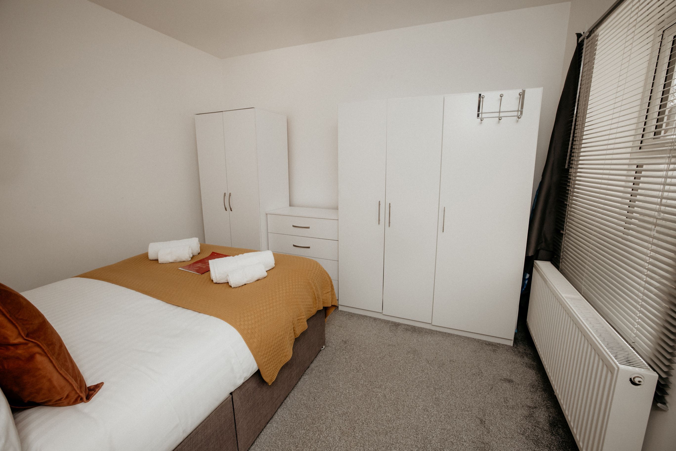 Un dormitorio con cama, armario, radiador y ventana con persianas.