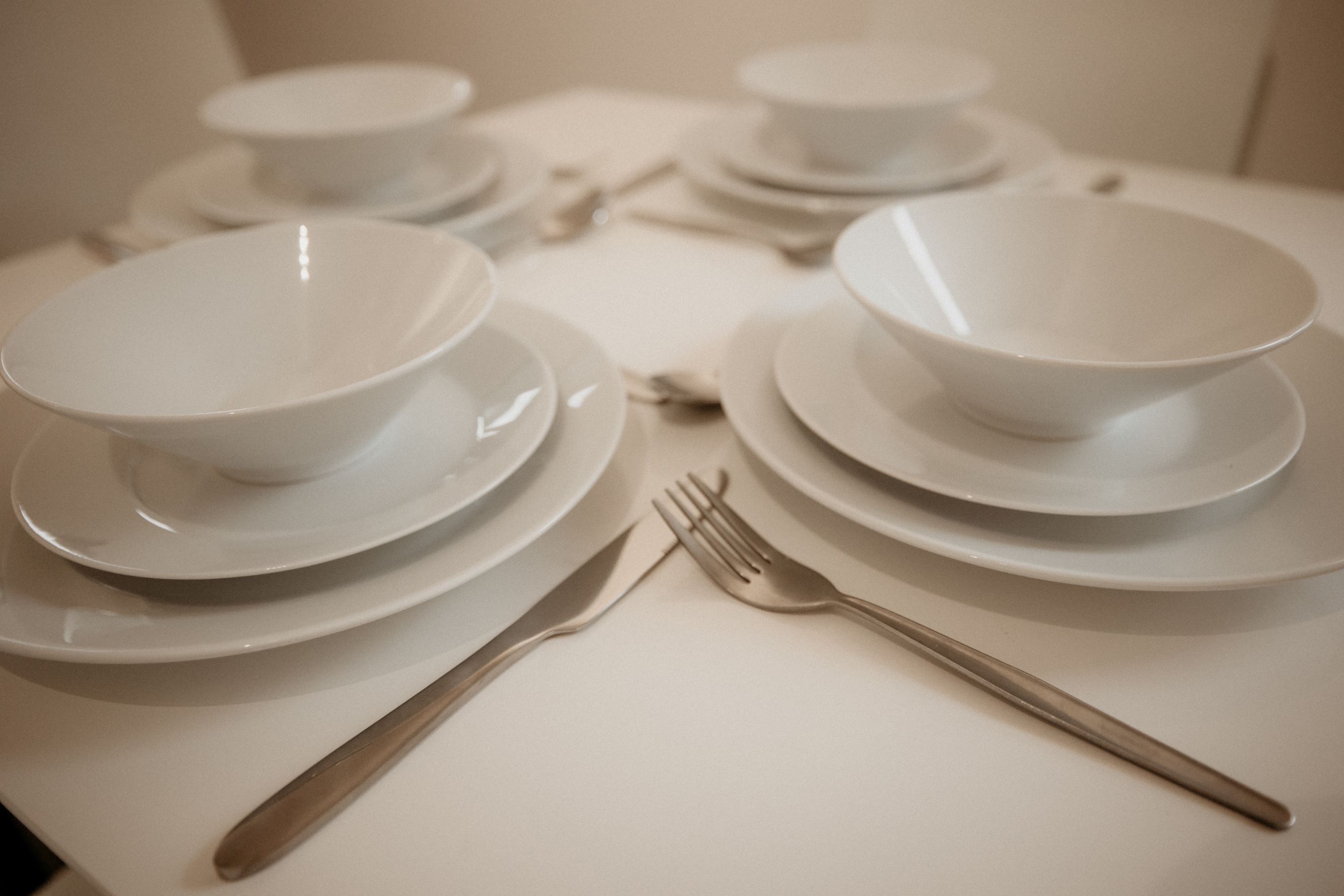 Une table dressée avec des assiettes, des bols et des couverts blancs.