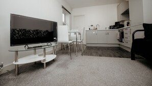 Um espaço compacto para viver, com televisão de tela plana, uma mesa de jantar e uma cozinha compacta.