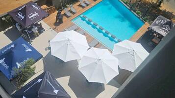 A rooftop pool area with lounge chairs and umbrellas, surrounded by a wooden deck and plants.