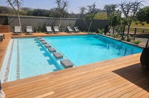 A rectangular swimming pool with a wooden deck and lounge chairs. - UMHLANGA Rocks Bookings apartment NEAR GATEWAY. (uMhlanga)