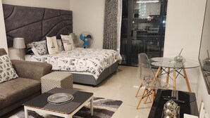A modern living room with a bed, sofa, coffee table, and a glass dining table. - UMHLANGA Rocks Bookings apartment NEAR GATEWAY. (uMhlanga)