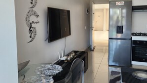 A modern kitchen with a stainless steel refrigerator, a built-in oven, and a flat-screen TV mounted on the wall. - UMHLANGA Rocks Bookings apartment NEAR GATEWAY. (uMhlanga)
