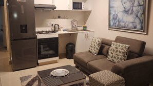 A compact living space with a kitchenette, a sofa, a coffee table, and a framed artwork on the wall. - UMHLANGA Rocks Bookings apartment NEAR GATEWAY. (uMhlanga)