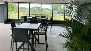 A spacious indoor area with a long table and chairs, large windows offering a view of greenery and buildings, and a potted plant. - UMHLANGA Rocks Bookings apartment NEAR GATEWAY. (uMhlanga)