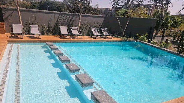 A rectangular swimming pool with a wooden deck and lounge chairs. - UMHLANGA Rocks Bookings apartment NEAR GATEWAY. (uMhlanga)