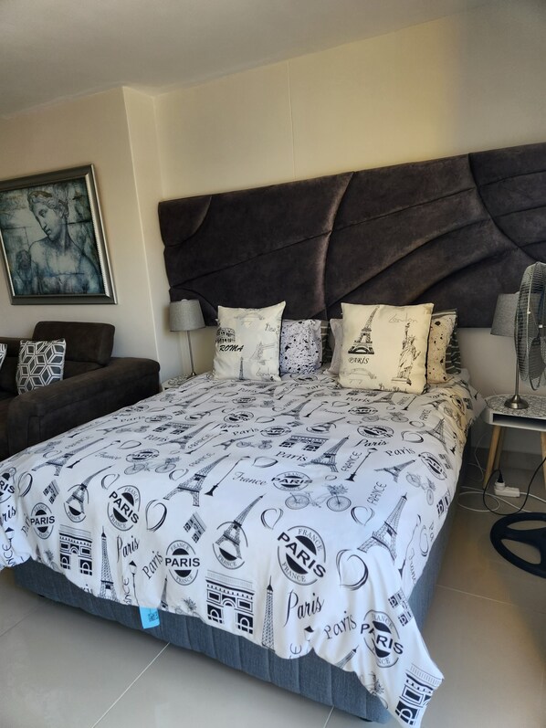 A bedroom with a large bed, a dark headboard, and a painting on the wall. - UMHLANGA Rocks Bookings apartment NEAR GATEWAY. (uMhlanga)