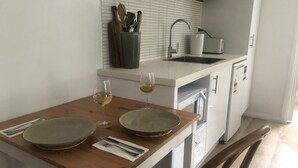 A compact kitchen with a wooden table set for two, two wine glasses, and a knife block. -  Tangara - A Stylish Newly Renovated Studio Apartment, close to the surf beach. (Inverloch)