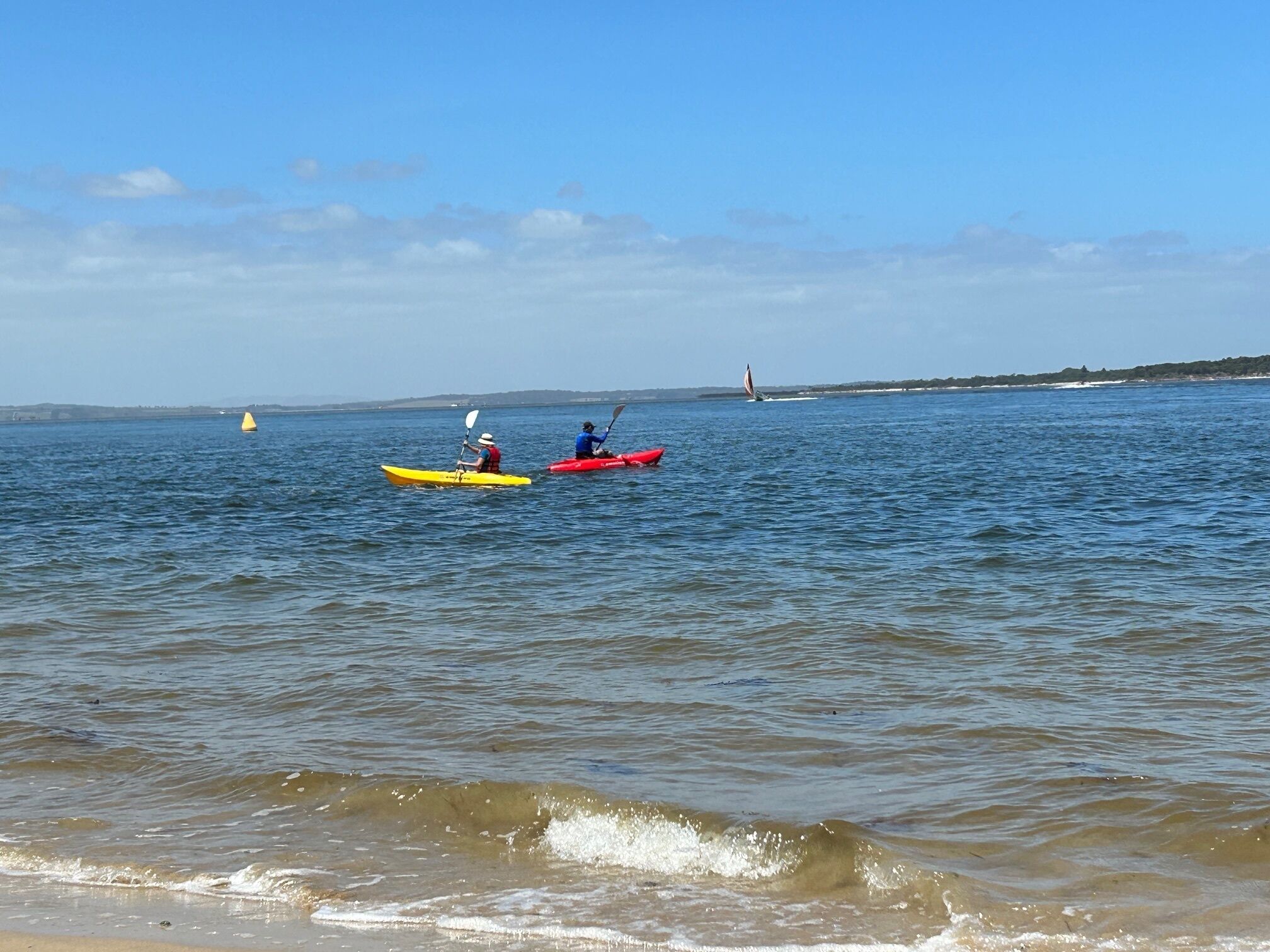 A calm sea with kayaks and a sailboat.