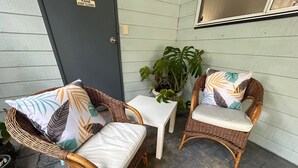 Two wicker chairs with cushions and a small white table on a patio with a dark door and a potted plant. -  Tangara - A Stylish Newly Renovated Studio Apartment, close to the surf beach. (Inverloch)