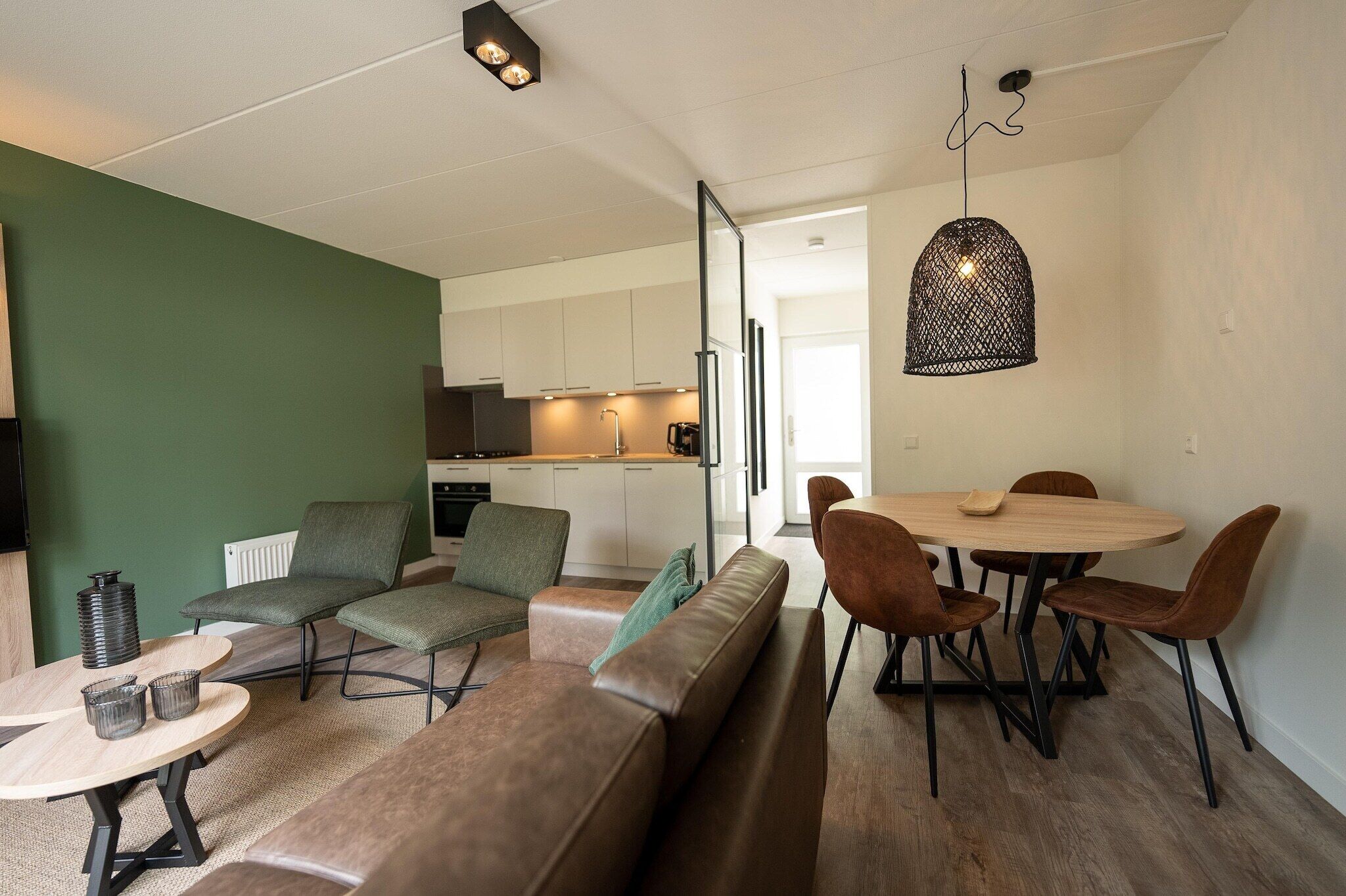 A modern living room with a green accent wall, a wooden dining table with brown chairs, and a sofa.