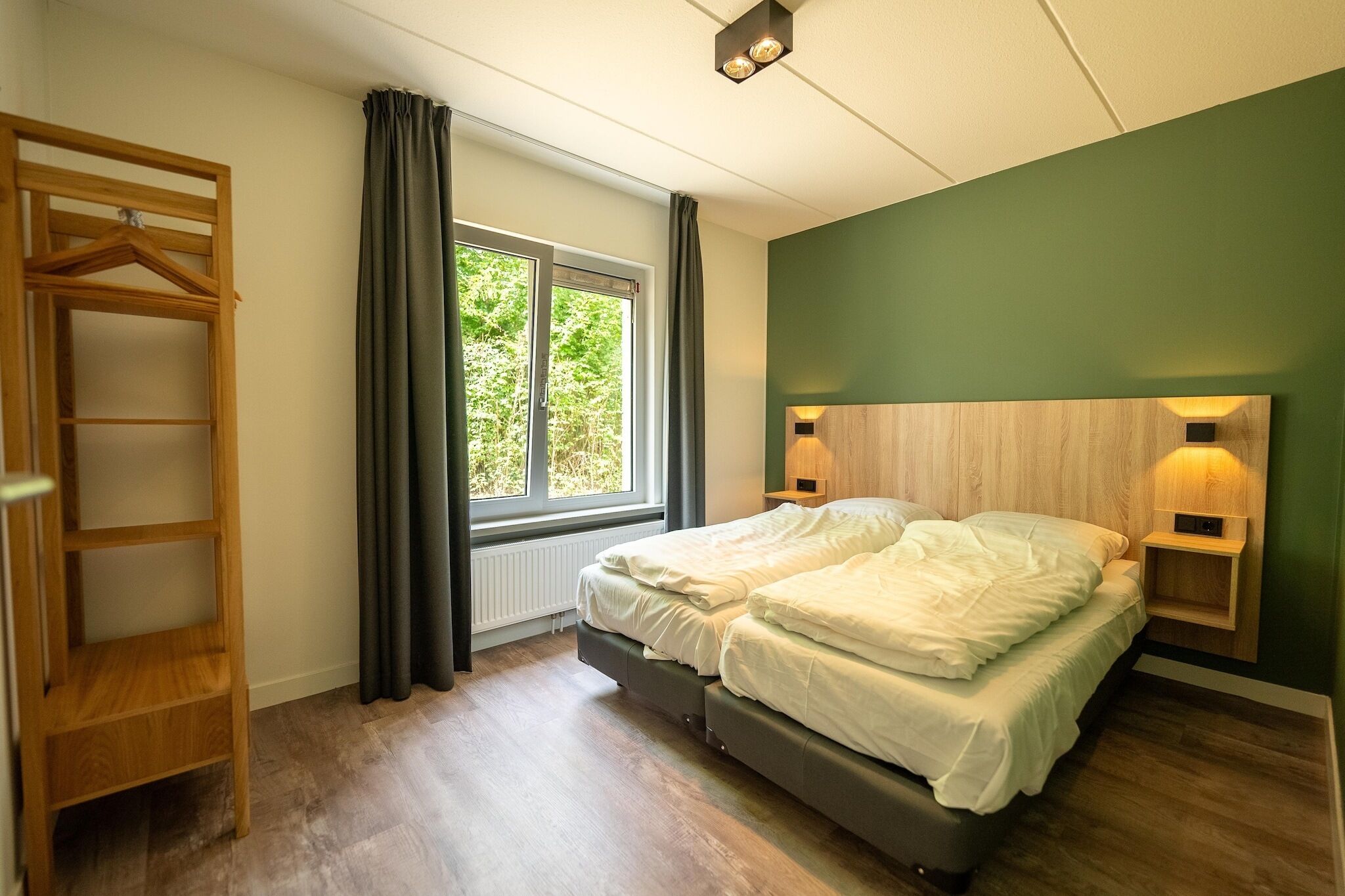 A bedroom with a bed, a wooden wardrobe, a window with curtains, and a wall-mounted light fixture.