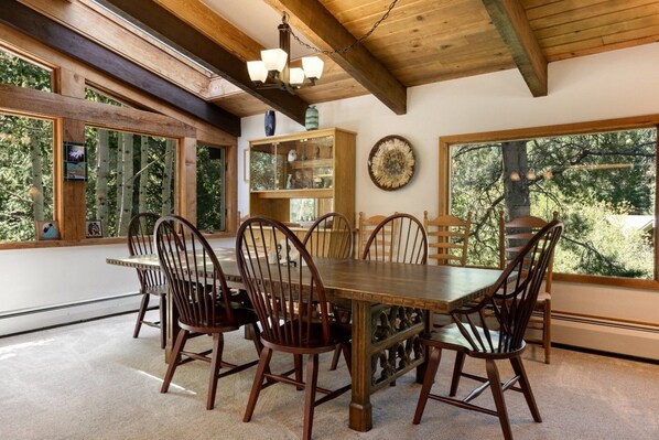 A dining area with a wooden table and chairs, large windows, and a ceiling with exposed beams. - Large East Vail Chalet - Hot Tub & Close to Bus (Vail)