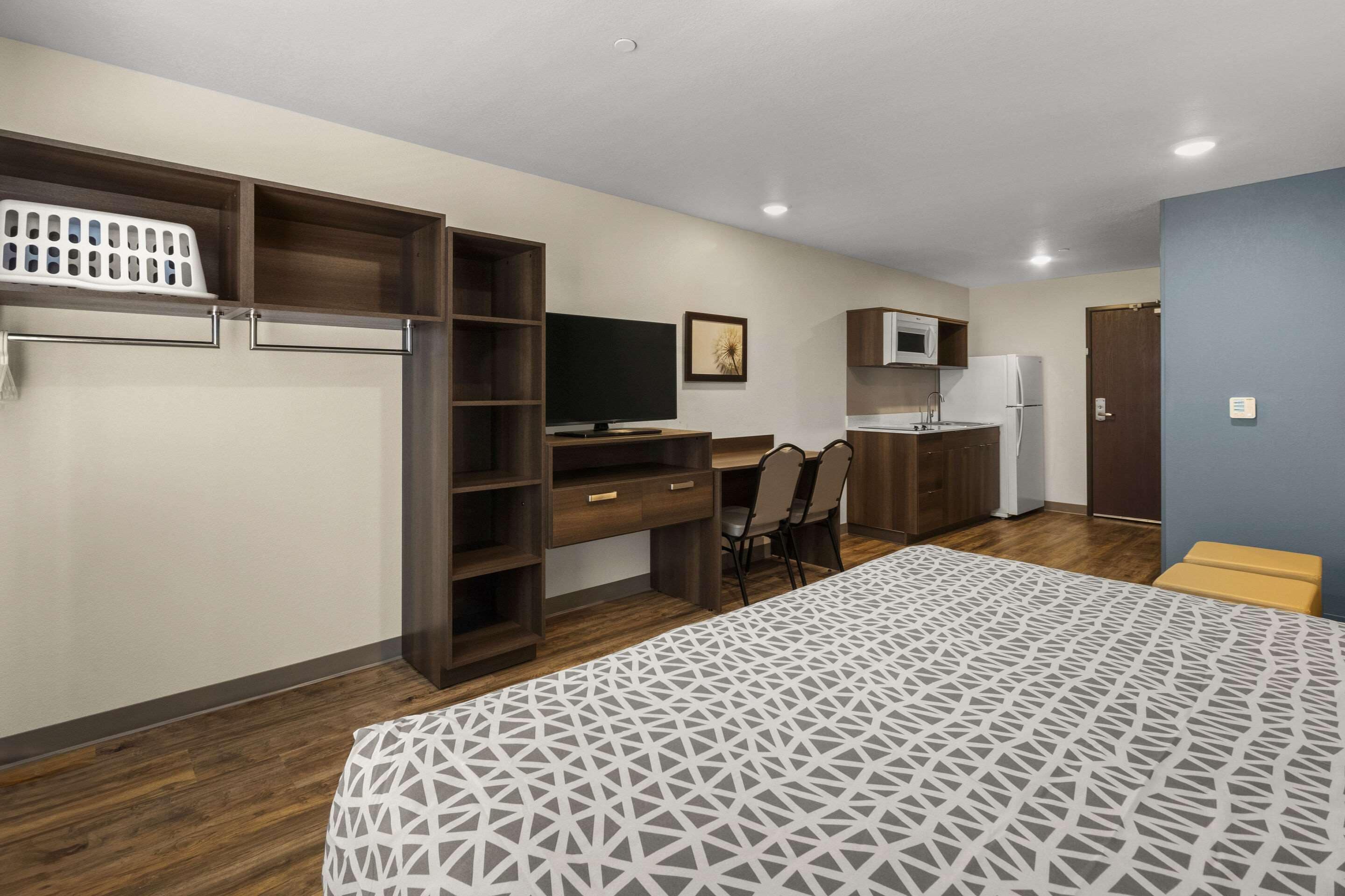 A bedroom with a bed, a desk, a chair, a TV, a microwave, and a refrigerator.