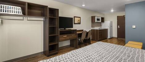 A bedroom with a bed, a desk, a chair, a TV, a microwave, and a refrigerator.