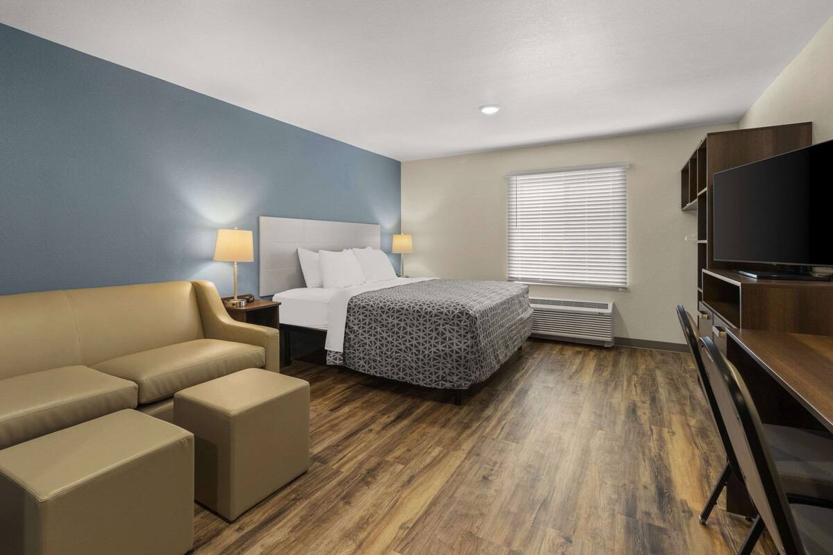 Habitación de hotel con cama, sofá, televisor y ventana con persianas.