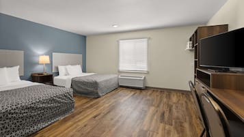 A hotel room with two beds, a TV, a desk, and a window with blinds.