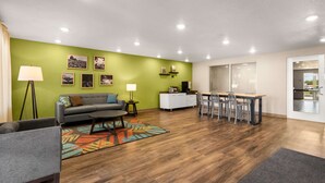 Un salon moderne avec un mur d’accent vert, un canapé gris, une table basse et un coin repas comprenant des chaises et une table.