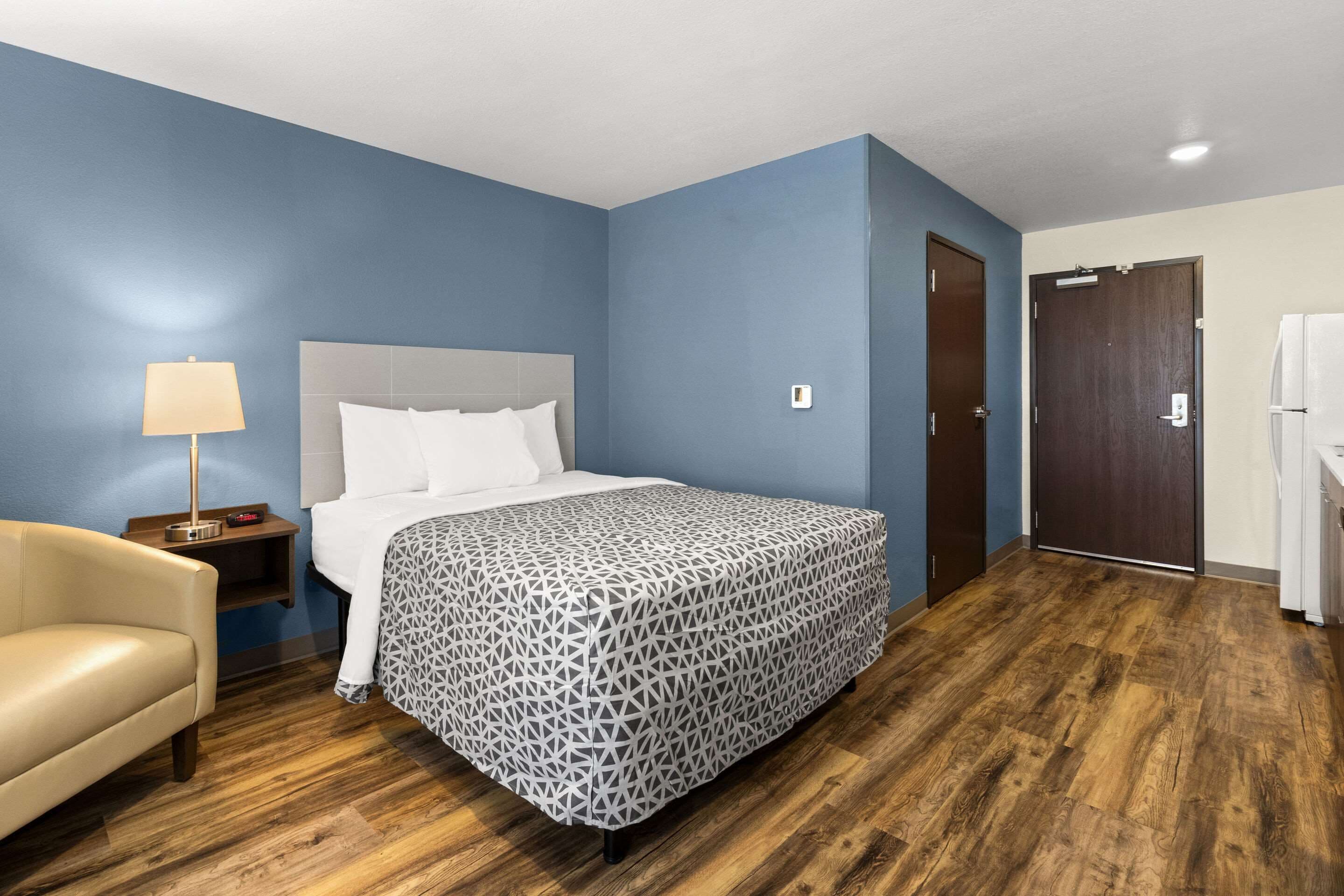Une chambre d’hôtel avec un lit, une table de chevet, une chaise et une porte.