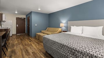 A hotel room with a bed, a desk, a chair, a lamp, and a door.