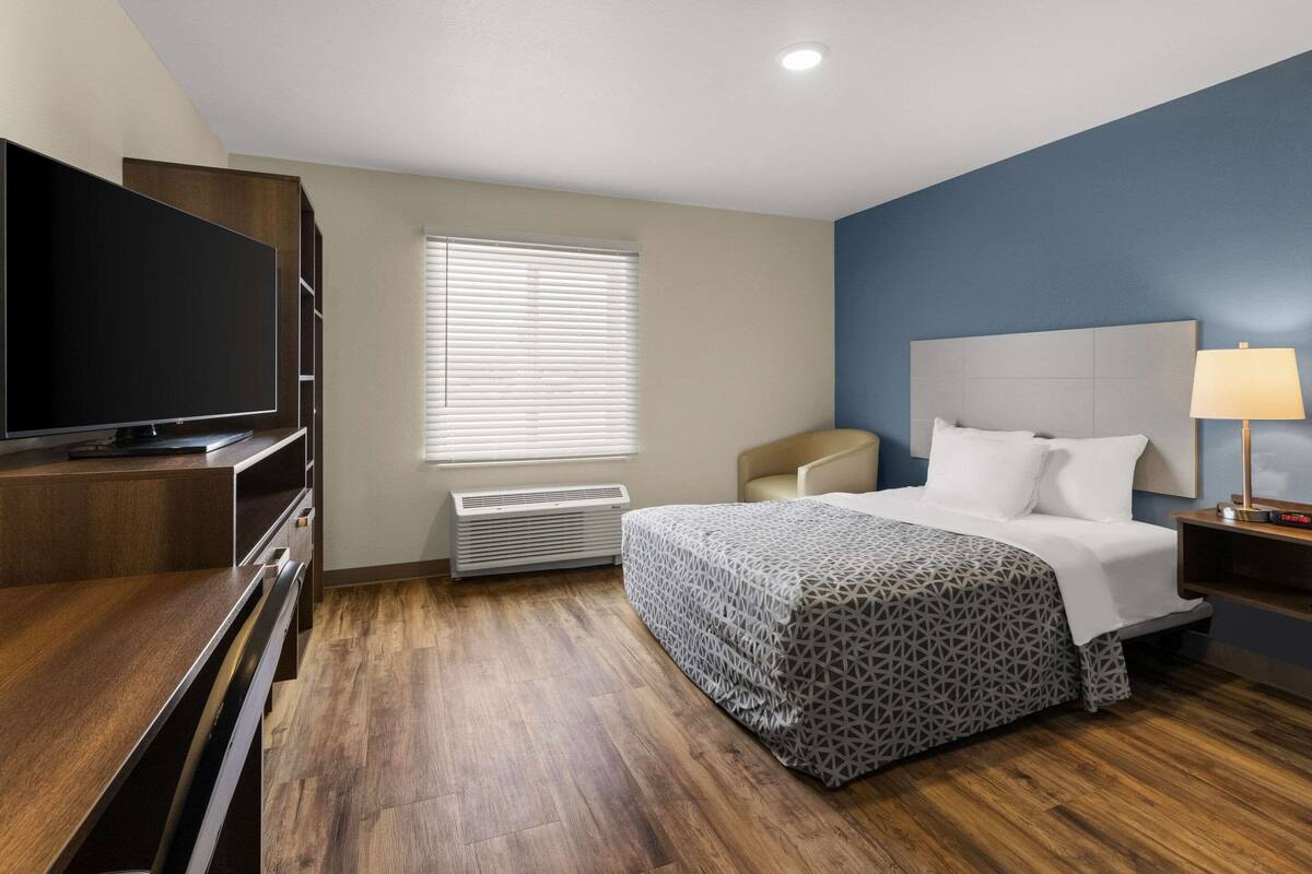 Habitación de hotel con cama, televisión, escritorio y ventana con persianas.