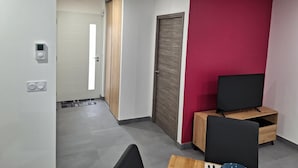 Una habitación de hotel moderna con una pared de acento roja, una puerta de madera, un televisor sobre un mueble de madera y un escritorio pequeño con una silla.