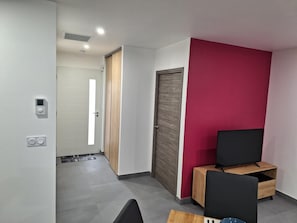 Moderni hotellihuone, jossa on punainen tehosteseinä, puuovi, televisio puupöydällä ja pieni työpöytä tuolilla.