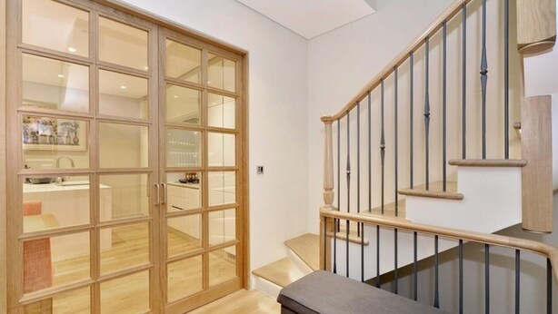 Uma escadaria com guarda-corpos de madeira e uma porta de vidro que dá para um espaço com cozinha.