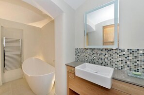 A modern bathroom with a freestanding bathtub, a large mirror, and a mosaic tile backsplash. - Charming 3-bed House in London (London)