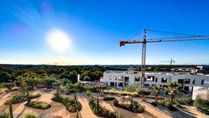 A modern building with a construction crane, surrounded by landscaped gardens and a clear sky. - Luxurous appartment with stunning views of the golfcourse and sea  (Orihuela Costa)