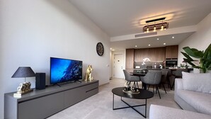 A modern living room with a flat-screen TV, a sofa, a coffee table, and a dining area with chairs. - Luxurous appartment with stunning views of the golfcourse and sea  (Orihuela Costa)