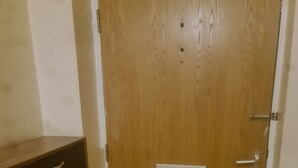 A wooden door with a handle and a lock, a small cabinet with drawers, and a light switch on the wall. - Remarkable 1-bed Apartment in Romford (Romford)