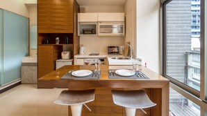 A modern kitchen with a dining area, featuring a wooden table, two bar stools, a microwave, and a sink. - 1B1b Cinema, Kitchen, Bathtub, Desk, 1.5min to MRT (Taipei City)