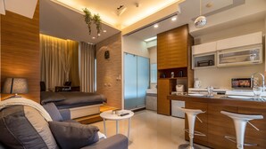 A modern living room with a sofa, a small round table, and a kitchen area with a microwave and bar stools. - 1B1b Cinema, Kitchen, Bathtub, Desk, 1.5min to MRT (Taipei City)