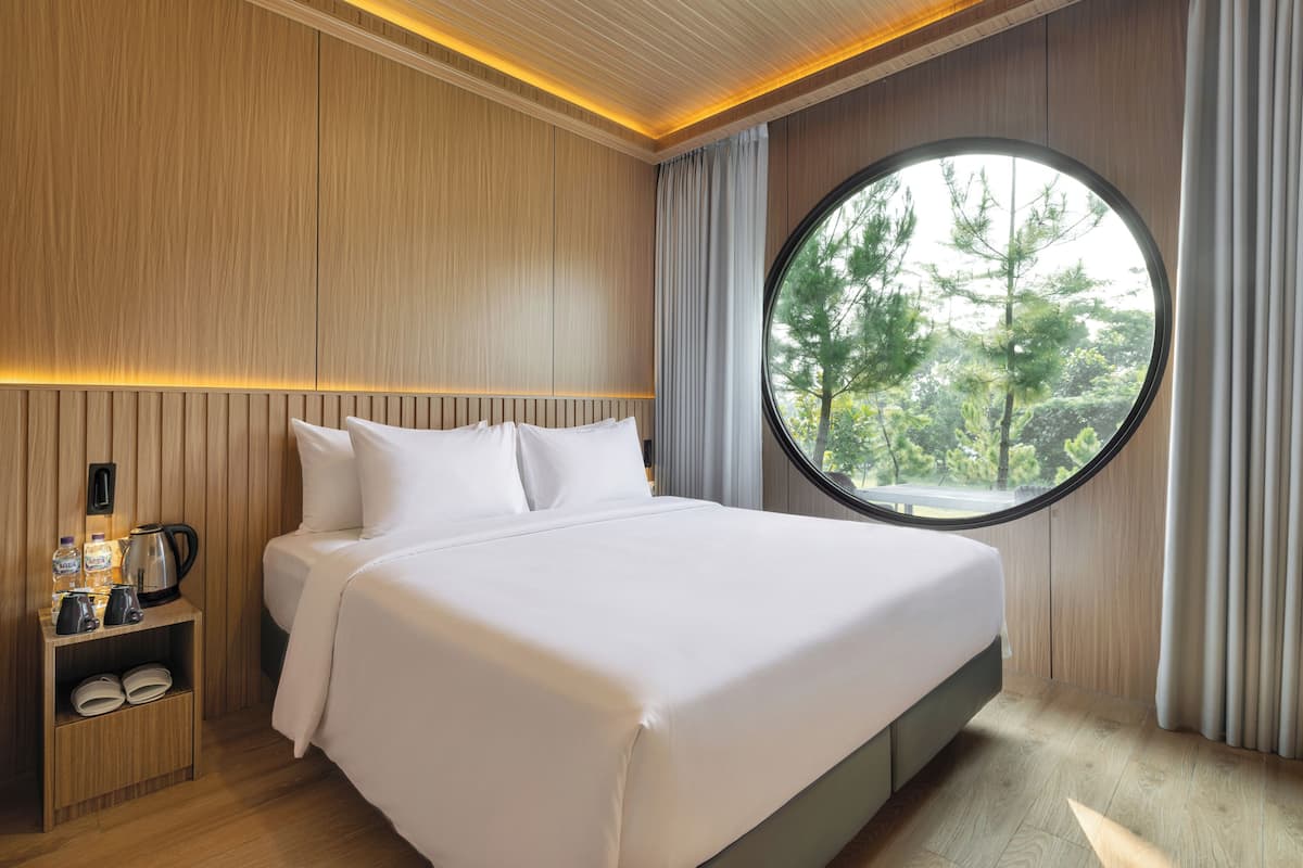 A modern hotel room with a large bed, a round window, and a nightstand with a kettle and coffee maker.