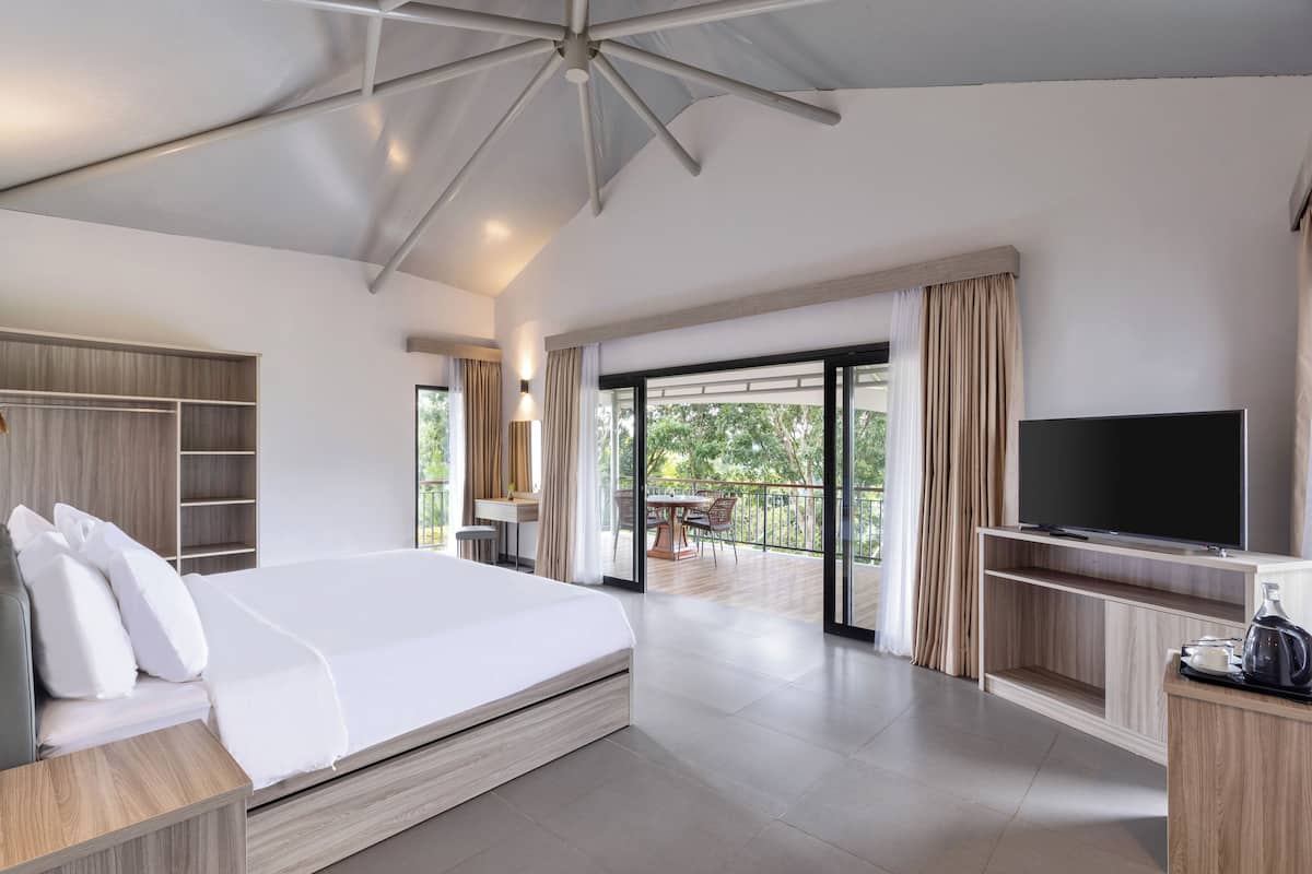 A modern hotel room with a large bed, a TV, a balcony, and a wooden wardrobe.