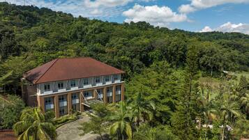 A multi-story building with a red-tiled roof, surrounded by lush greenery and palm trees.