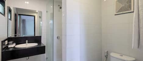 Un baño moderno con ducha de vidrio, lavamanos con encimera negra y inodoro blanco.