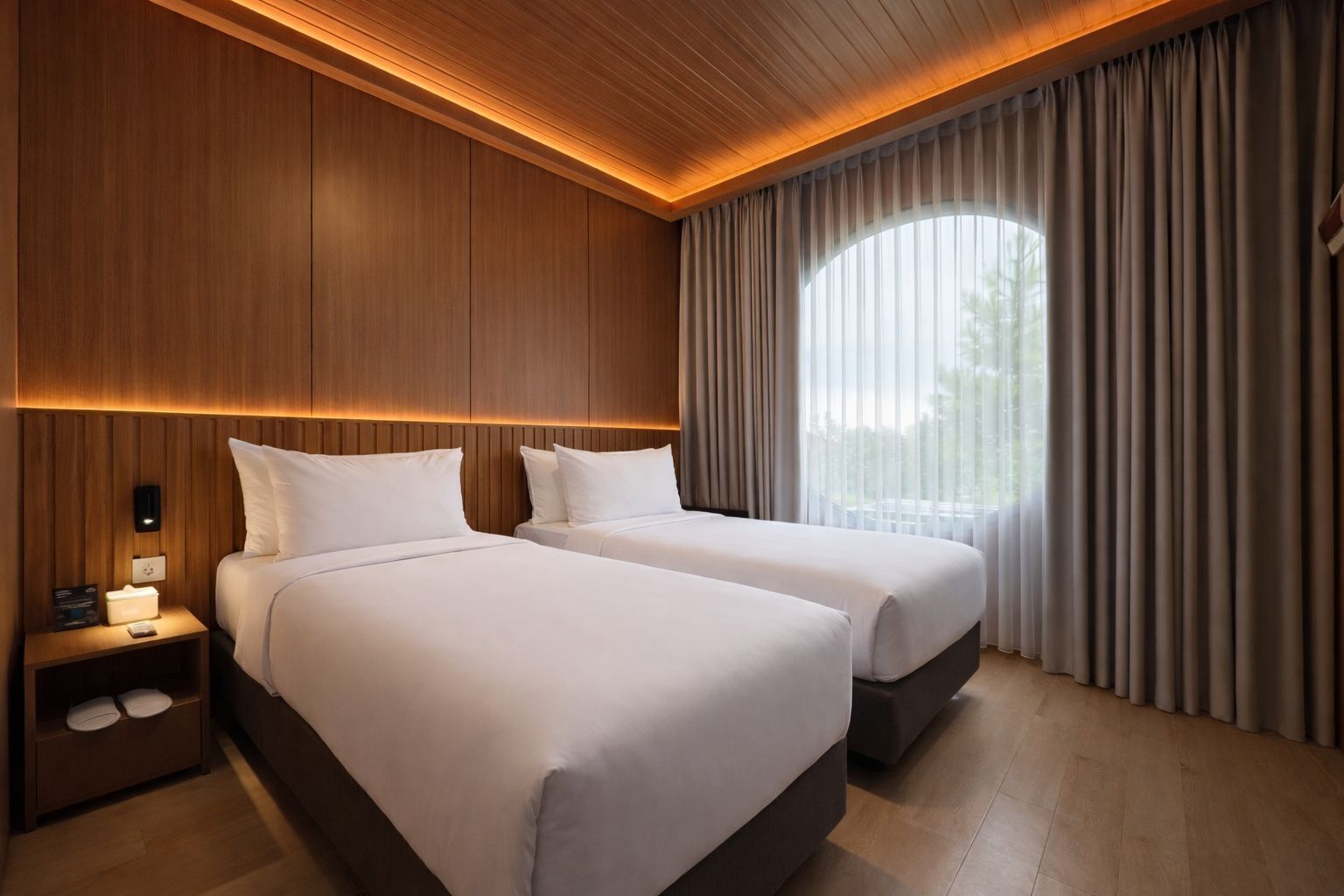 A hotel room with two beds, wooden paneling, a nightstand with a lamp, and a large window with curtains.