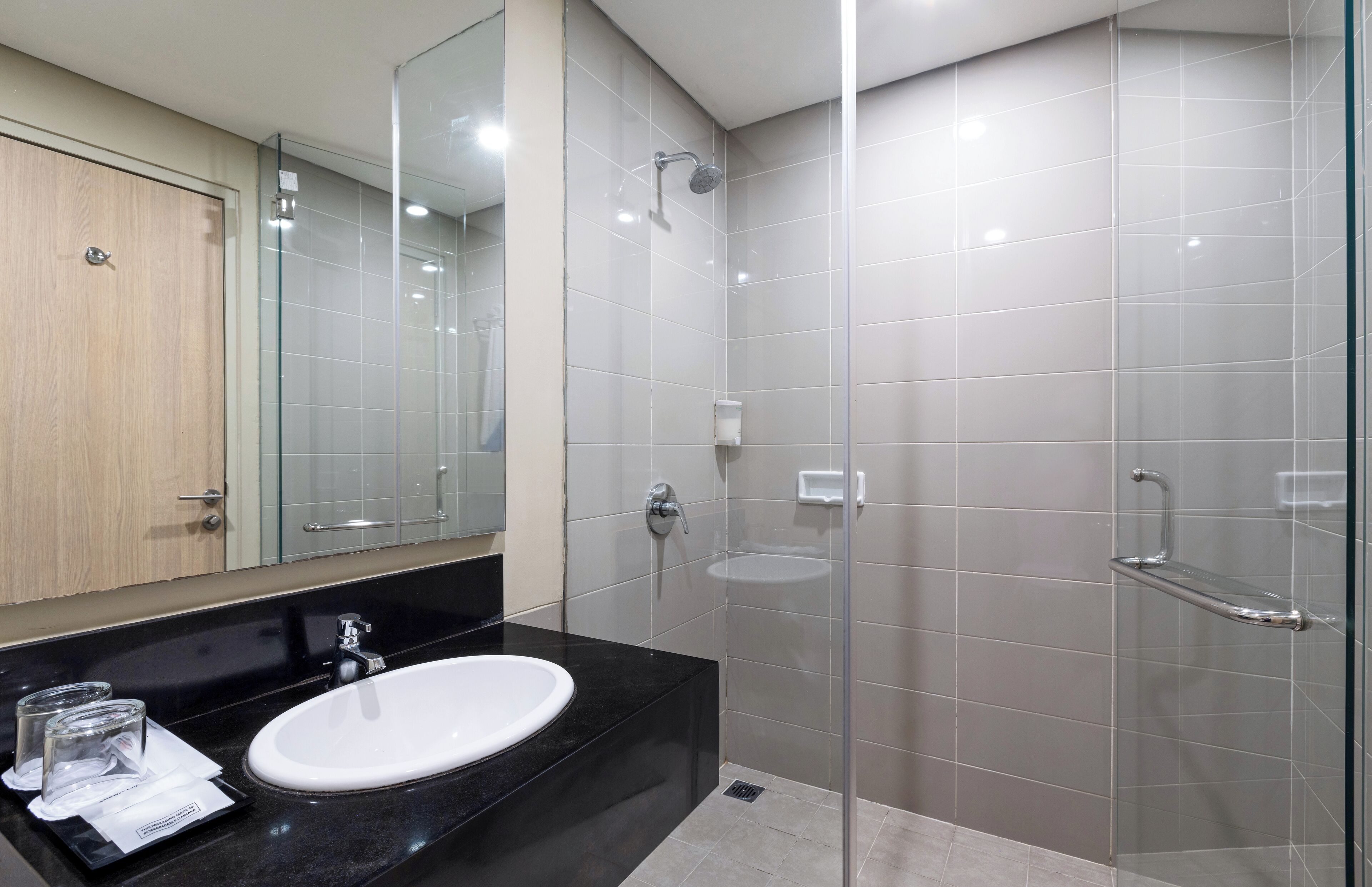 Un baño moderno con encimera negra, lavabo blanco y cabina de ducha de vidrio.