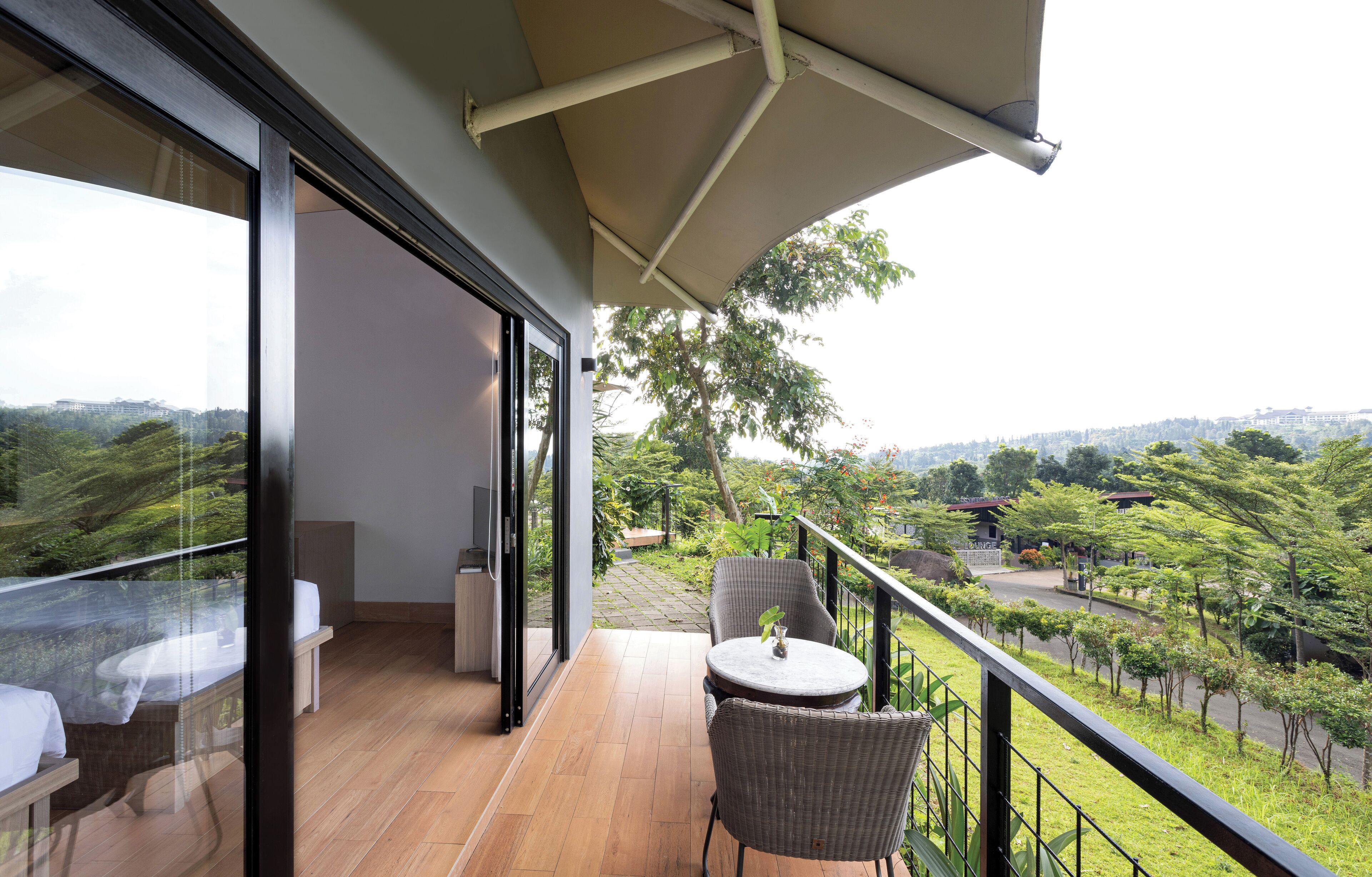 Un balcon doté d’un plancher en bois, de deux fauteuils en osier, d’une petite table et d’une paroi en verre.