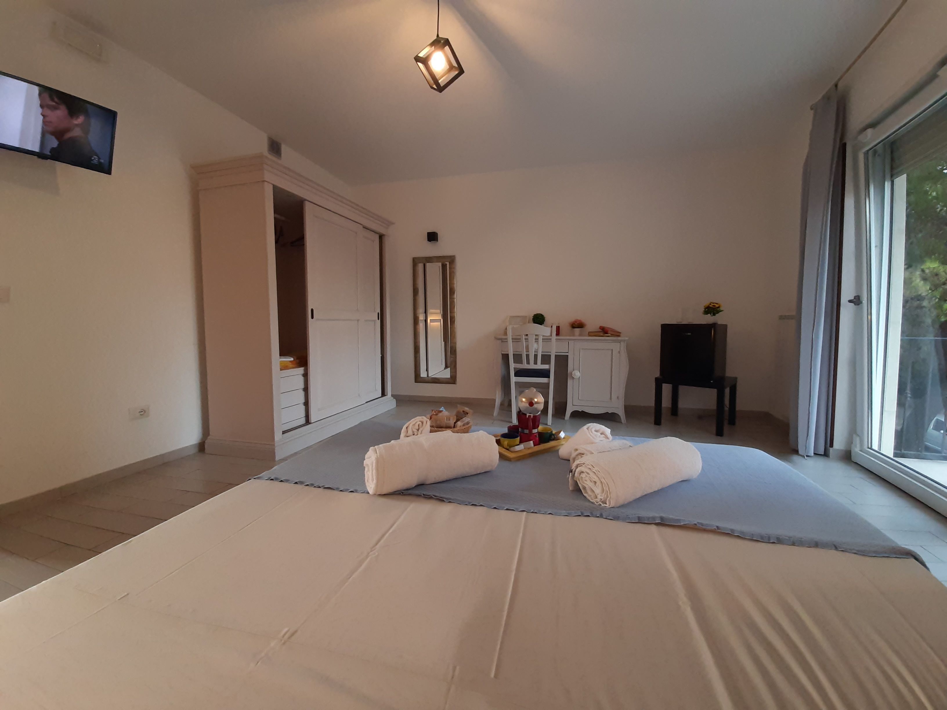 Une chambre spacieuse avec un grand lit, un bureau, une chaise et un téléviseur fixé au mur.