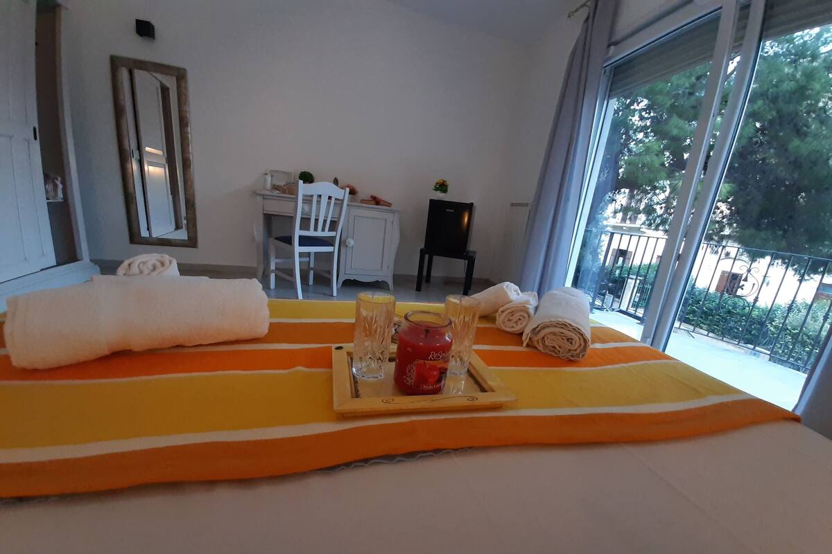 A hotel room with a bed, a desk, a chair, and a window with a view of trees.