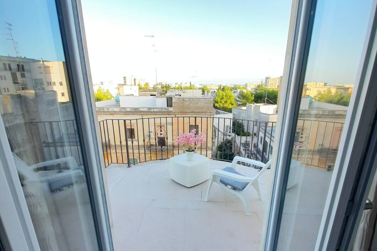 A balcony with a white chair and a small table with a flower vase.